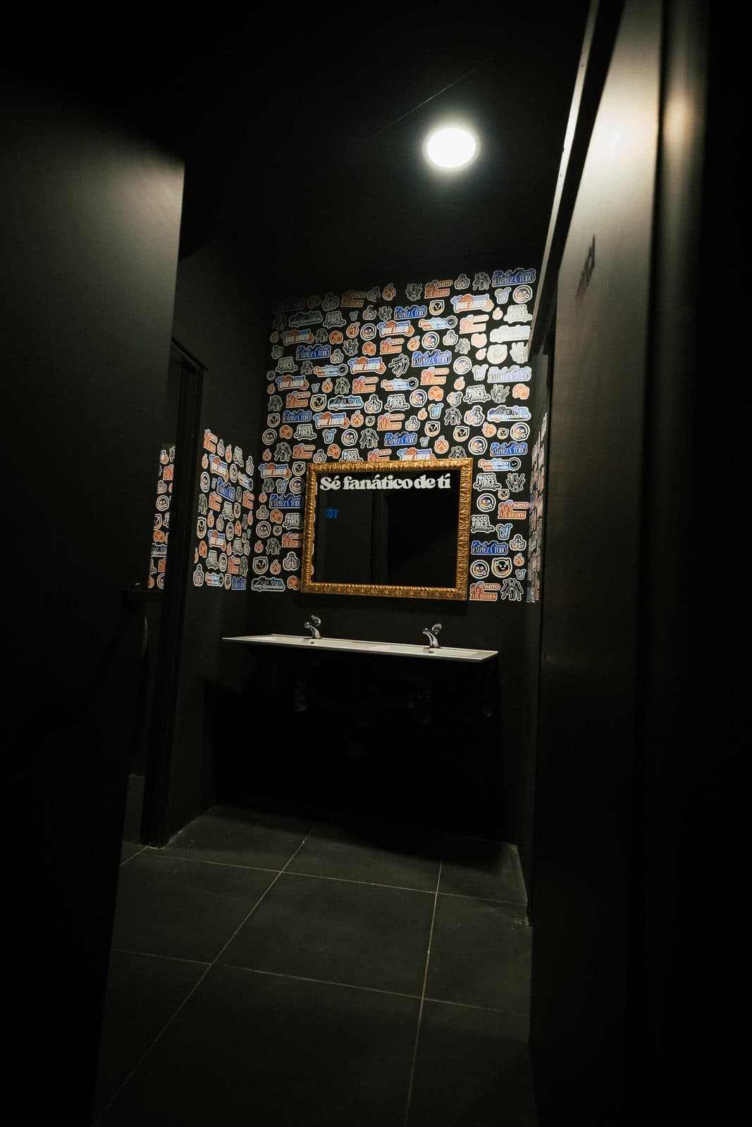 El baño, con la pared de pegatinas y el espejo dorado